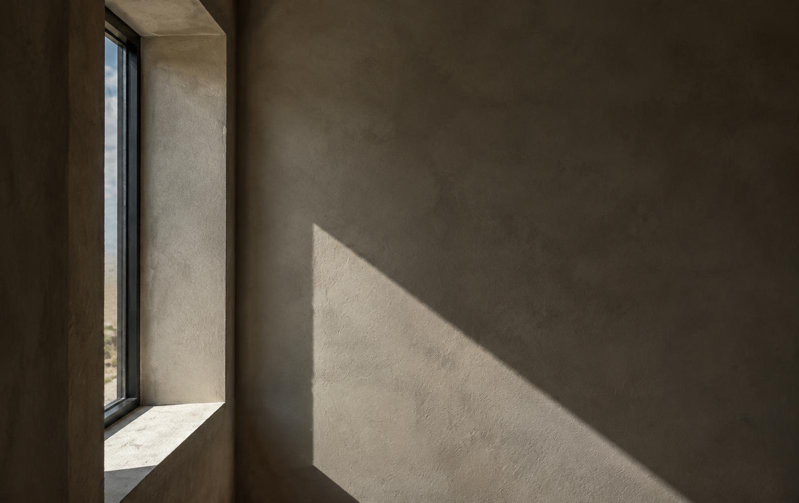 Lime plaster wall with a deep window reveal and hard afternoon shadow